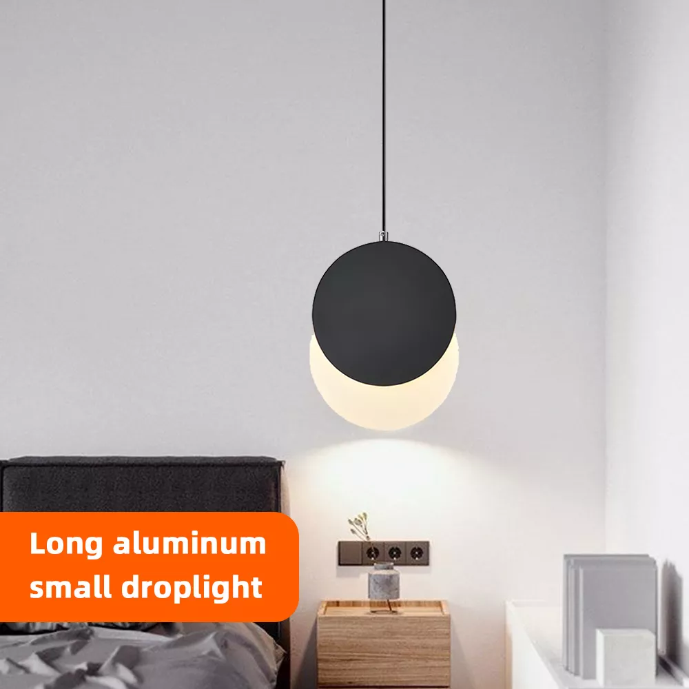Black globe pendant lamp hanging beside a bed with warm LED light illumination