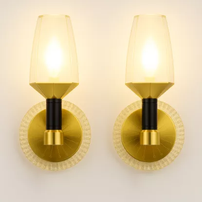 Modern gold and black crystal wall sconces with amber glow, mounted on white wall