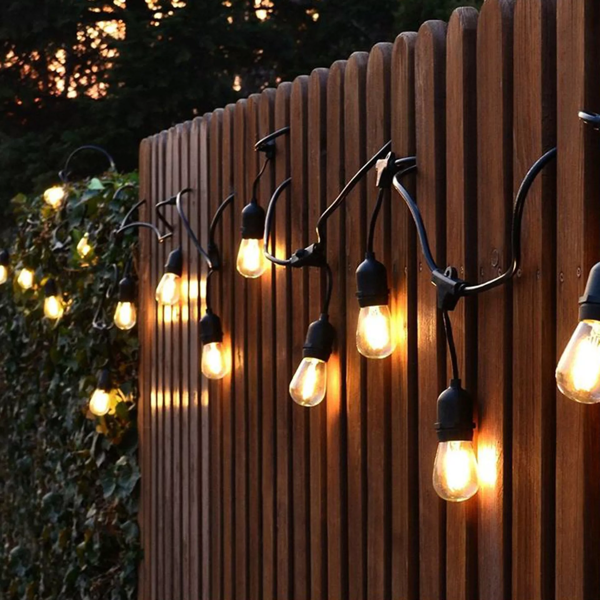 Warm outdoor string lights hanging on fence creating cozy garden ambiance