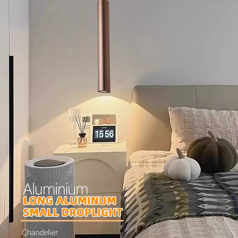 Long aluminum LED pendant droplight installed in modern bedroom, minimalist hanging chandelier providing focused warm lighting above bedside area.